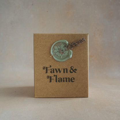 Fawn & Flame candle presented in a kraft paper box, stamped with vegan ink and eco-friendly sage wax seal, ensuring our packaging is as thoughtful as our candle.